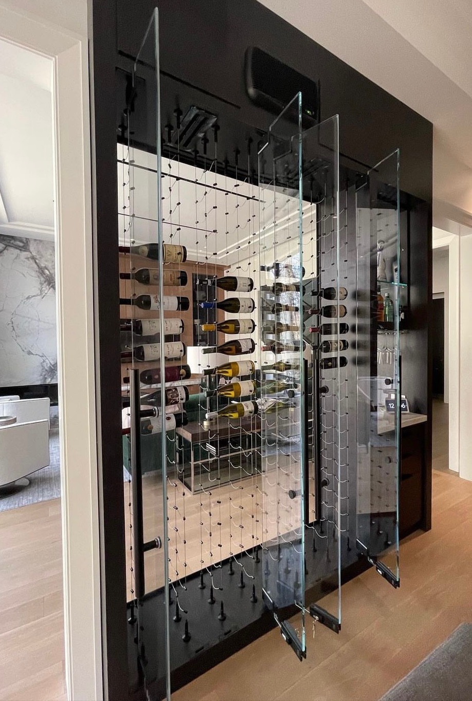 Glass wine cellar system with clear panels, black frame, and integrated bottle storage